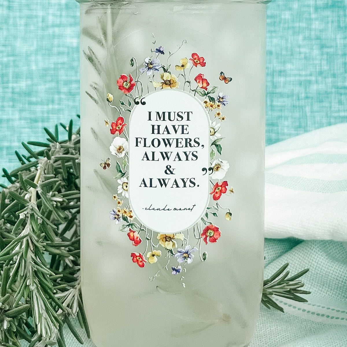 Close up of a mason jar tumbler that says "I must have flowers, always & always. -Claude Monet” with flowers creating an oval around the quote.