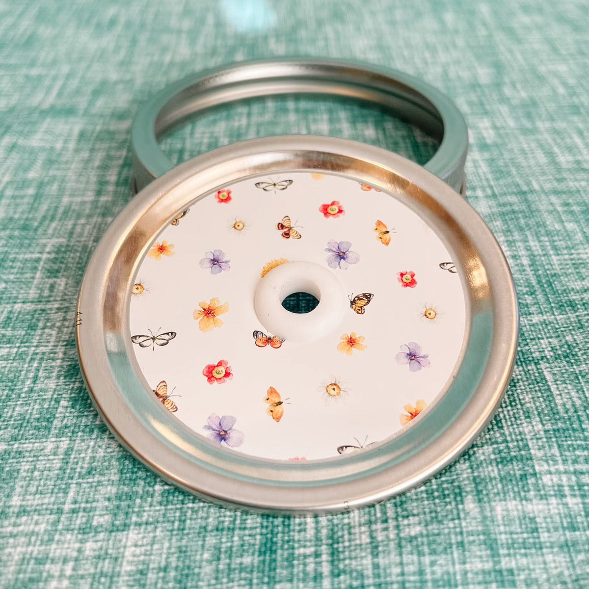 straw lid with a white background, there are flowers and butterflies arranged in a grid-like pattern