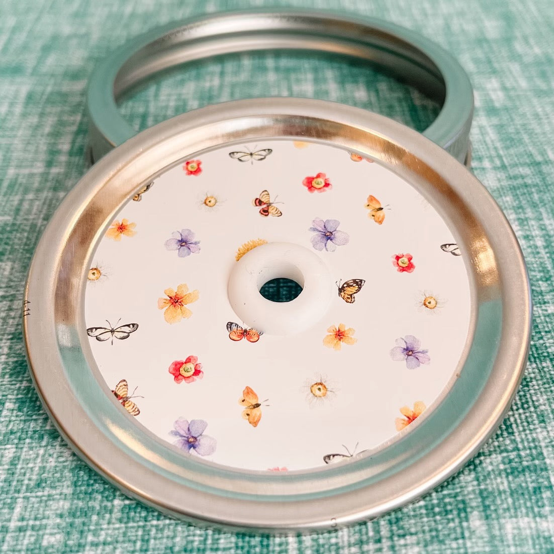 close up of a straw lid with a white background, there are flowers and butterflies arranged in a grid-like pattern
