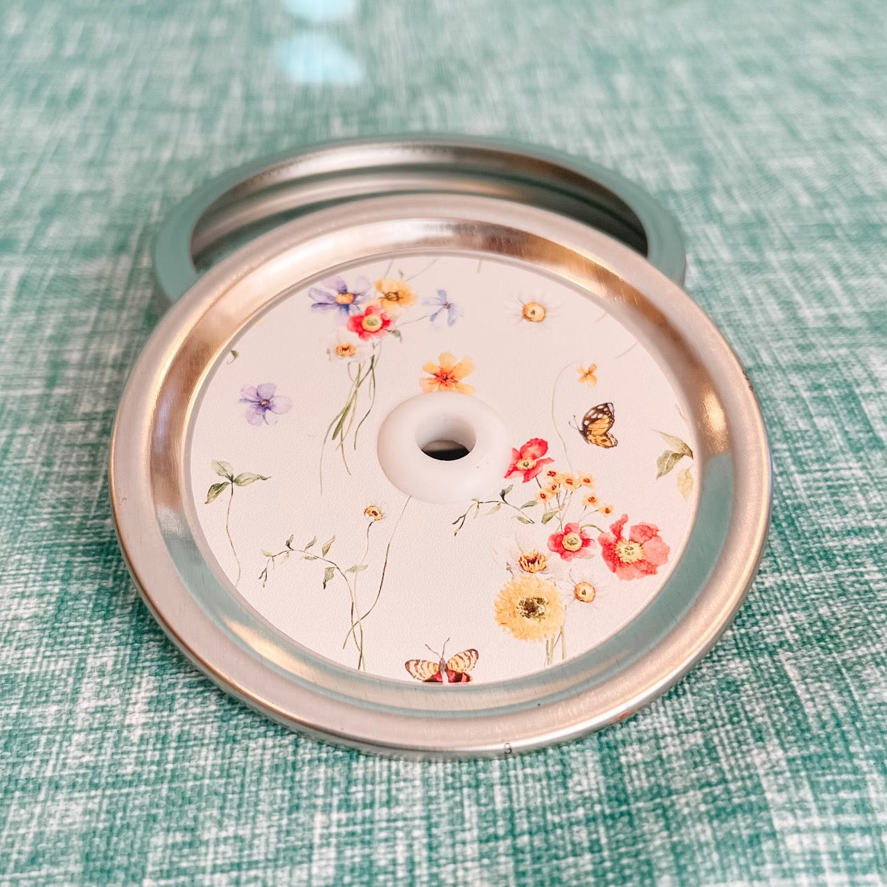 straw lid with a pale green background, bundles of flowers, butterflies, and leaves sparsely scattered