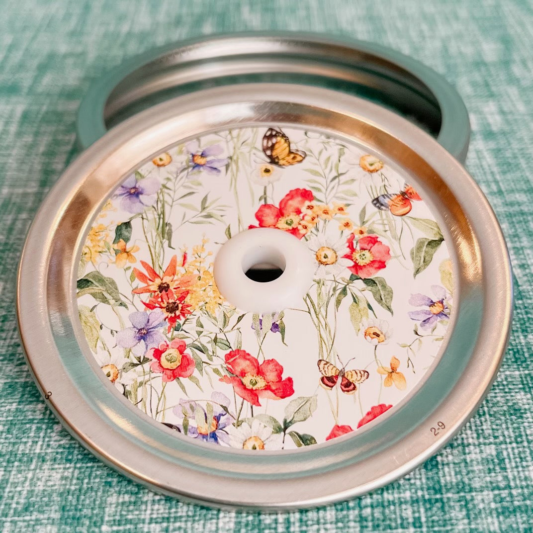 close up of a straw lid with a white background, cluttered with leaves, flowers, and butterflies