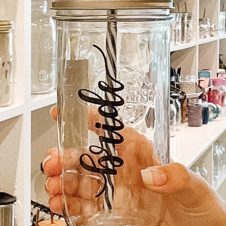 Close up of a hand holding a mason jar tumbler that has “bride” written on it in script vertically.