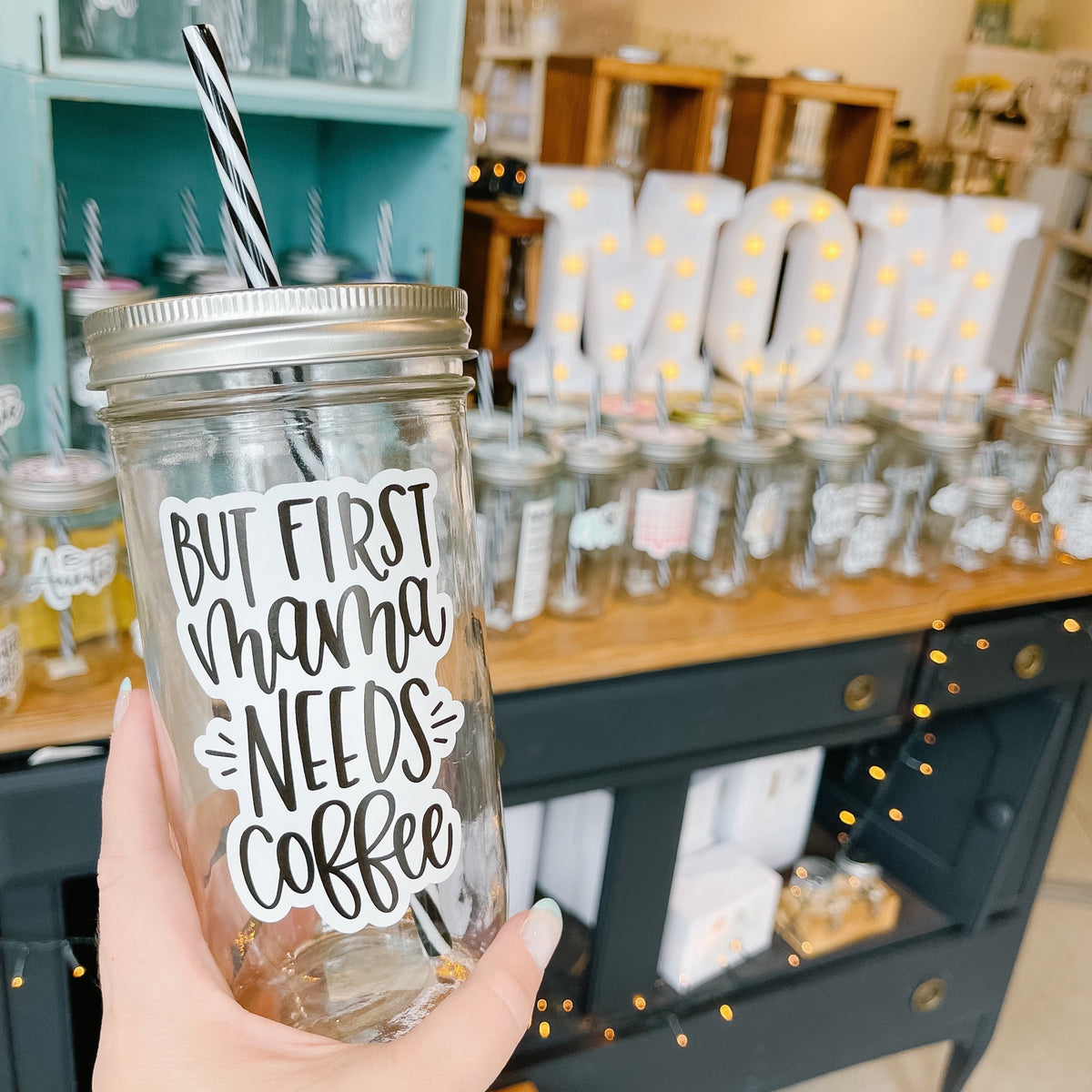 Hand holding a mason jar tumbler that says “but first mama needs coffee”