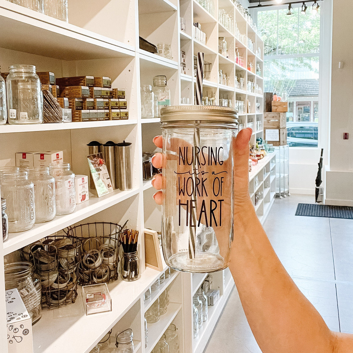 Hand holding a mason jar tumbler that says “nursing it’s a work of heart”