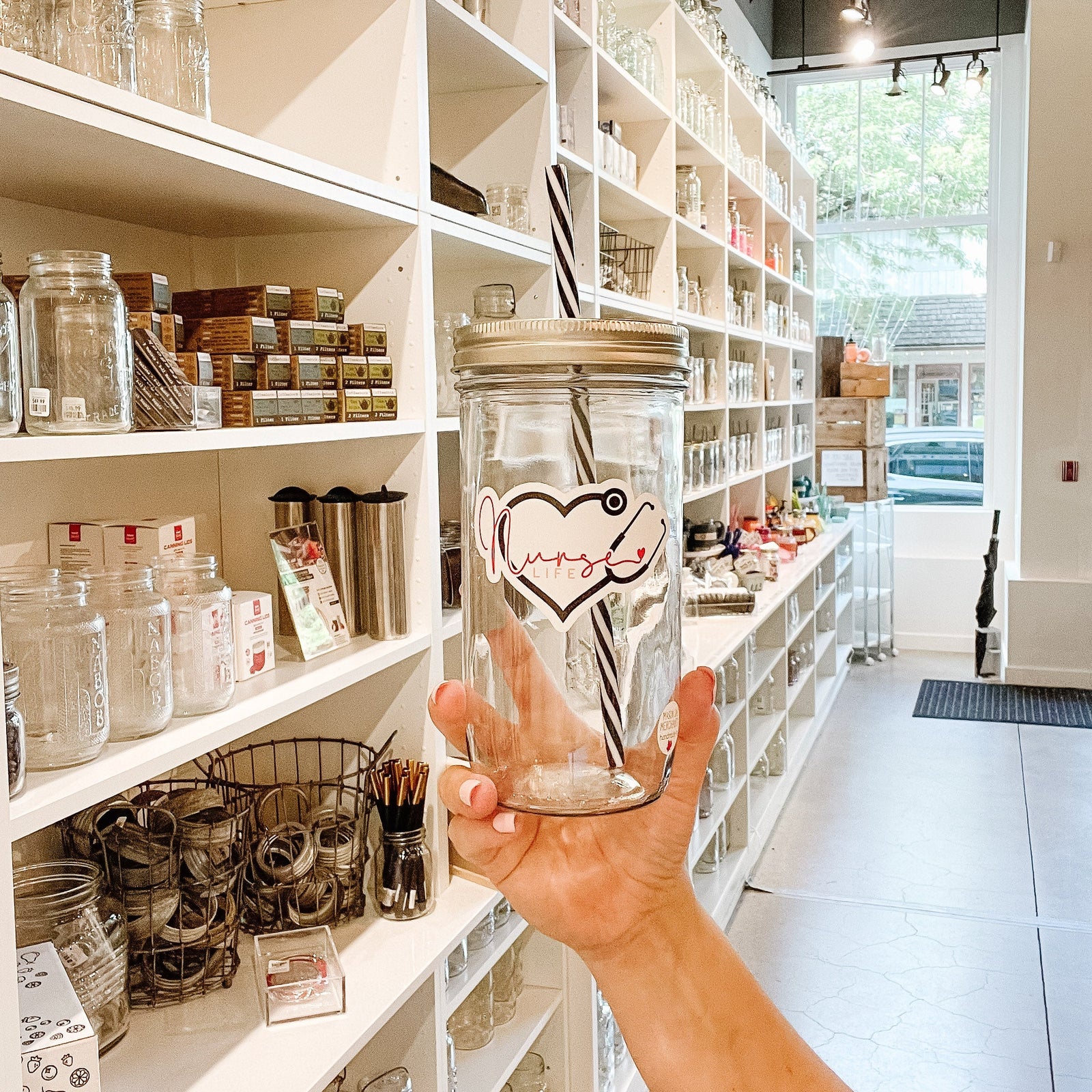 Hand holding a mason jar tumbler that says "nurse life” within a heart made out of a stethoscope