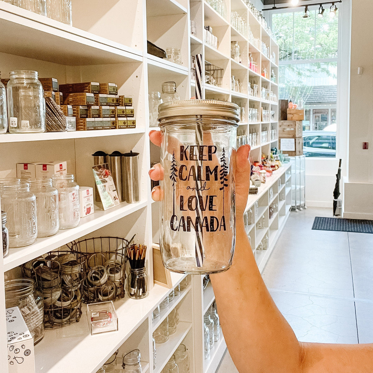 Hand holding a mason jar tumbler that says “Keep calm and love Canada” with a skinny tree on either side of the words
