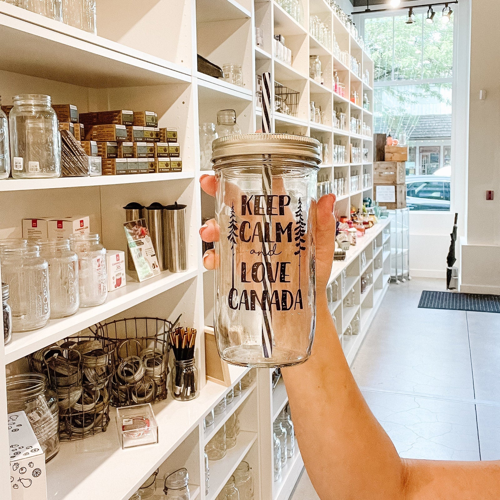 Hand holding a mason jar tumbler that says “Keep calm and love Canada” with a skinny tree on either side of the words
