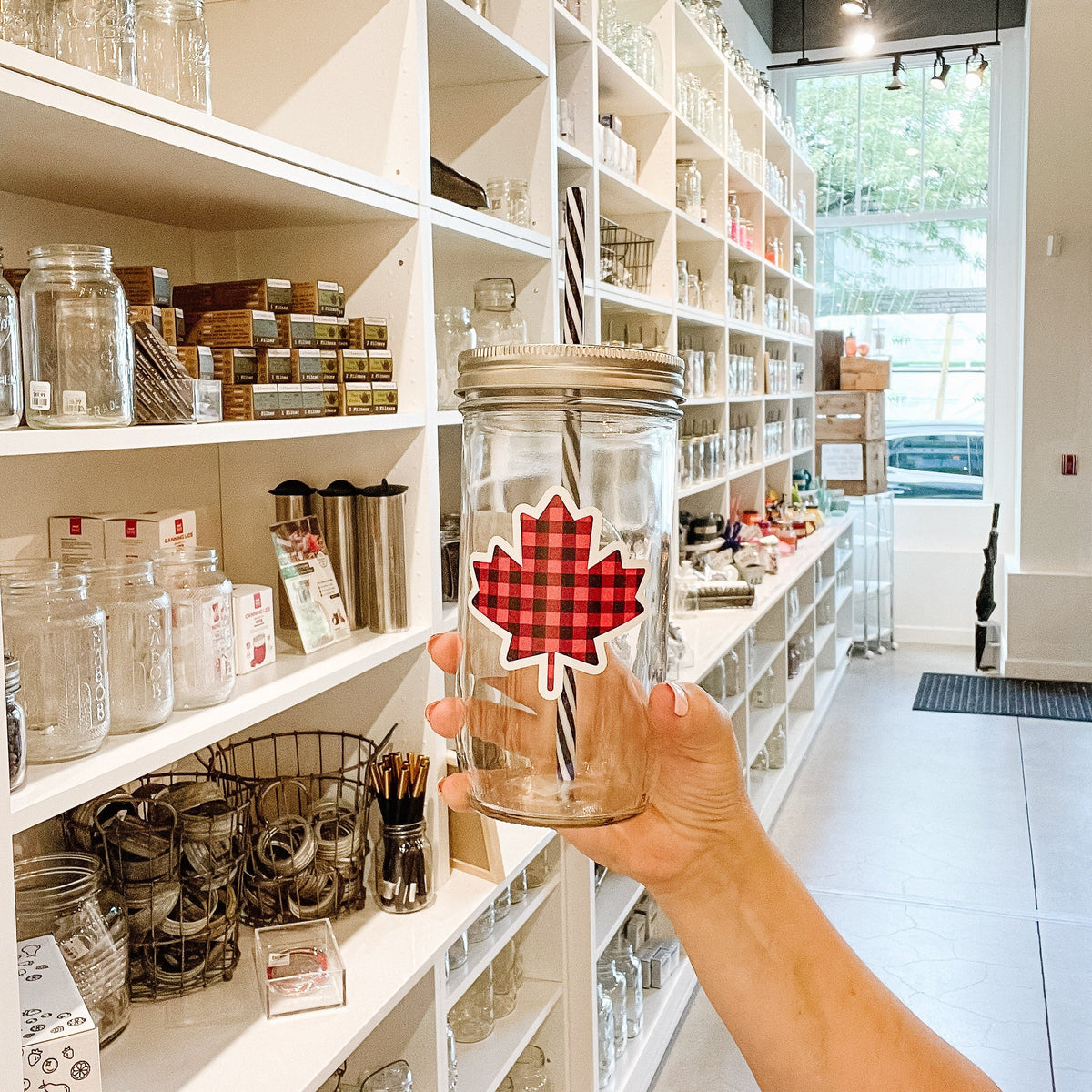 Hand holding a mason jar tumbler that has a maple leaf on it in a black and red plaid pattern.