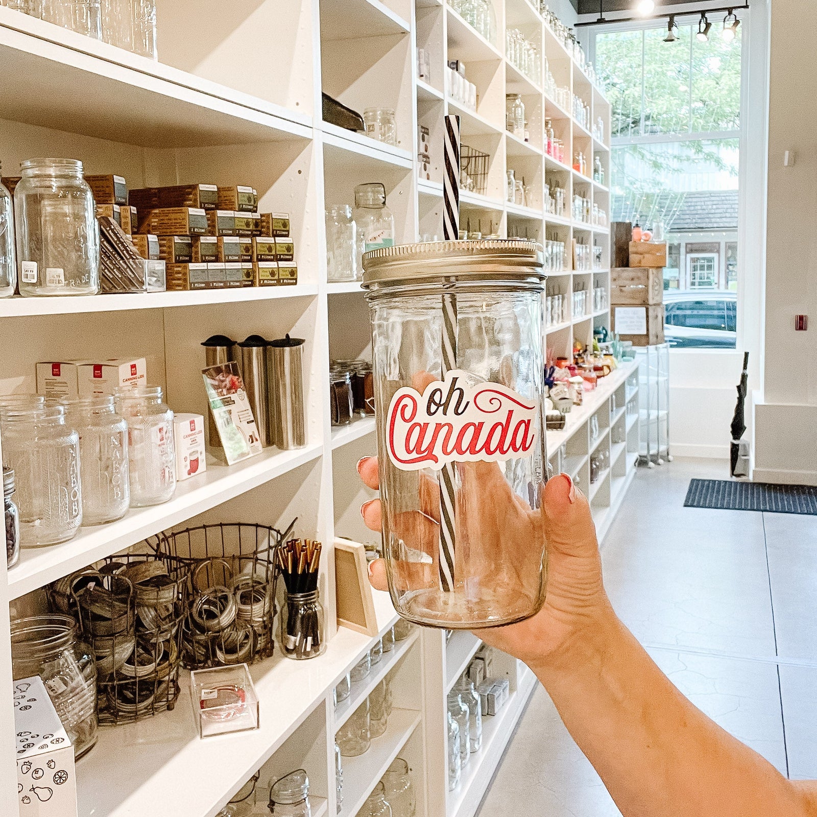 Hand holding a mason jar tumbler that says “oh Canada” in black and red