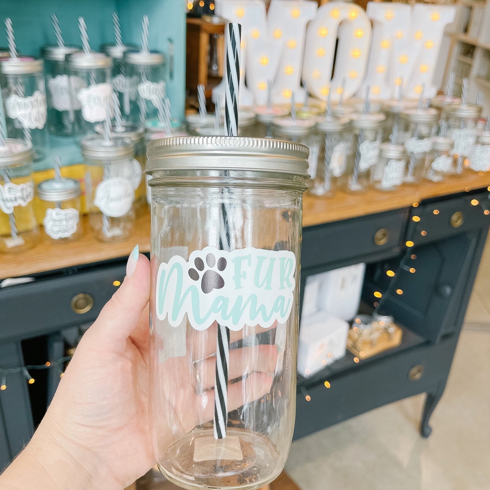Hand holding a mason jar tumbler that says “fur mama” in teal with a small black paw print.