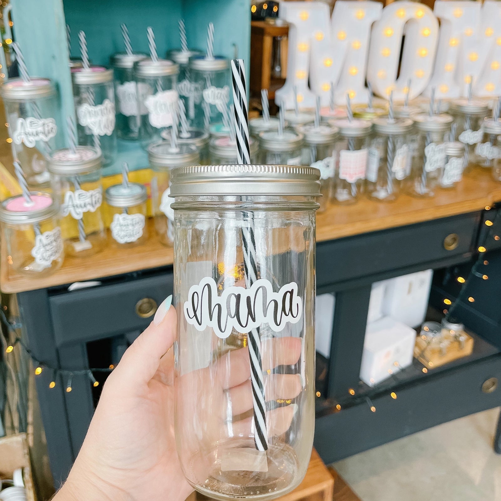 Hand holding a mason jar tumbler that says “mama” in black script on a white background