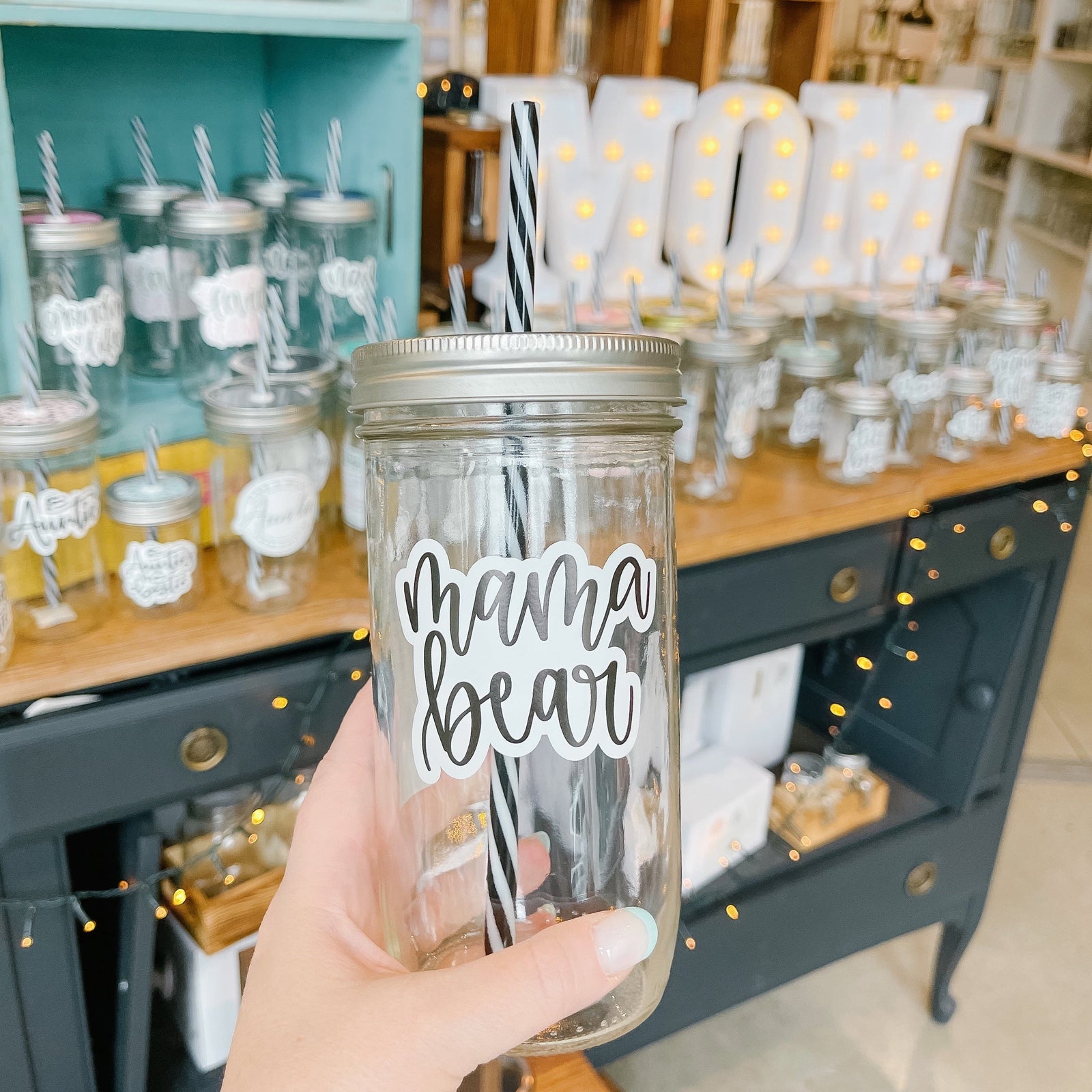 Hand holding a mason jar tumbler that says "mama bear” in black script on a white background
