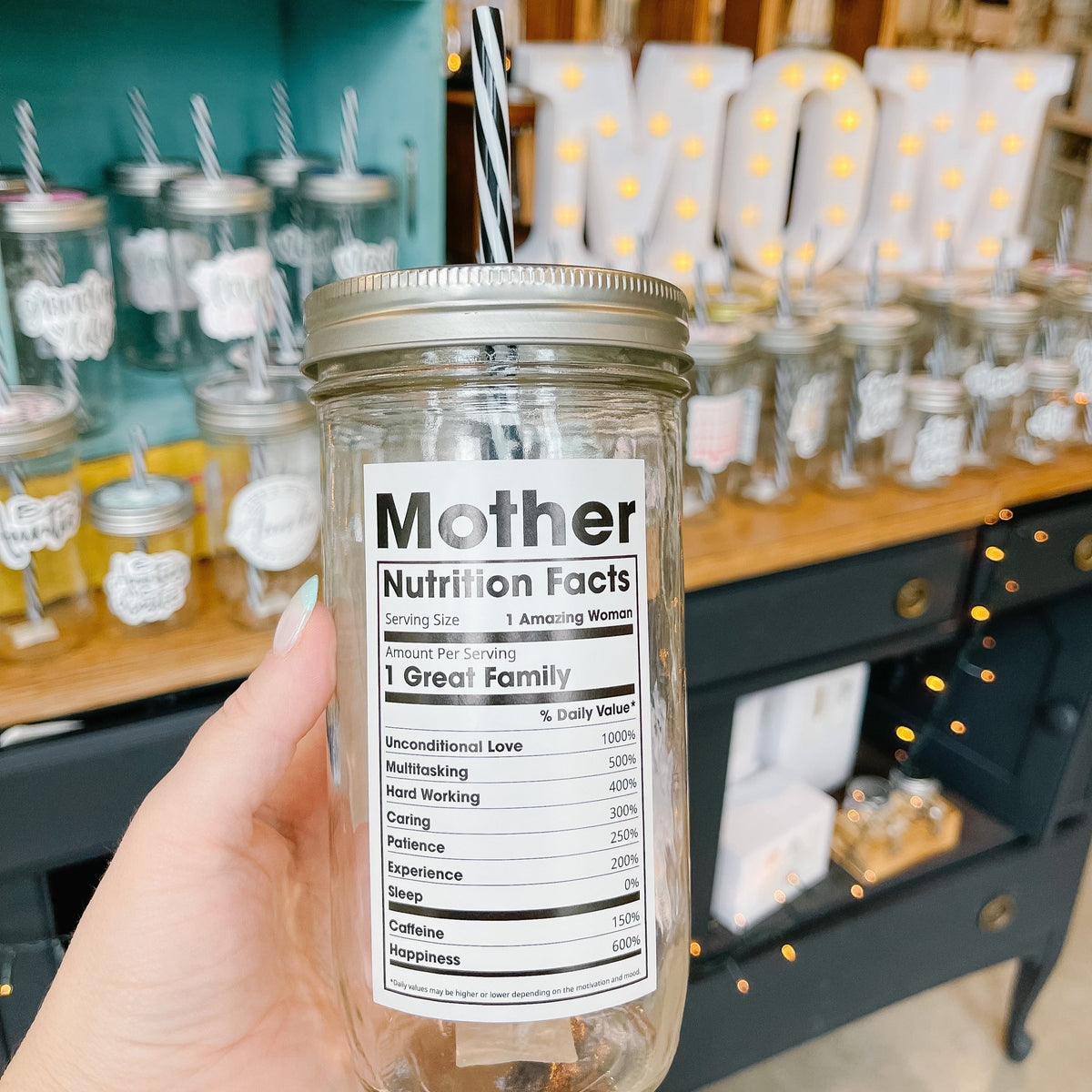 Hand holding a mason jar tumbler that has a “mother nutritional facts” decal