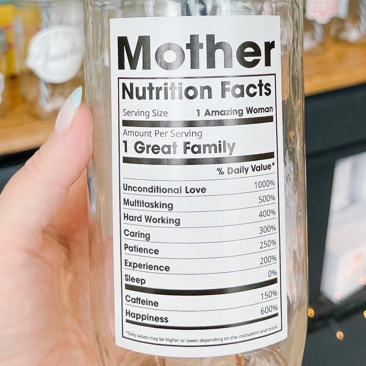 Close up of a hand holding a mason jar tumbler that has a “mother nutritional facts” decal