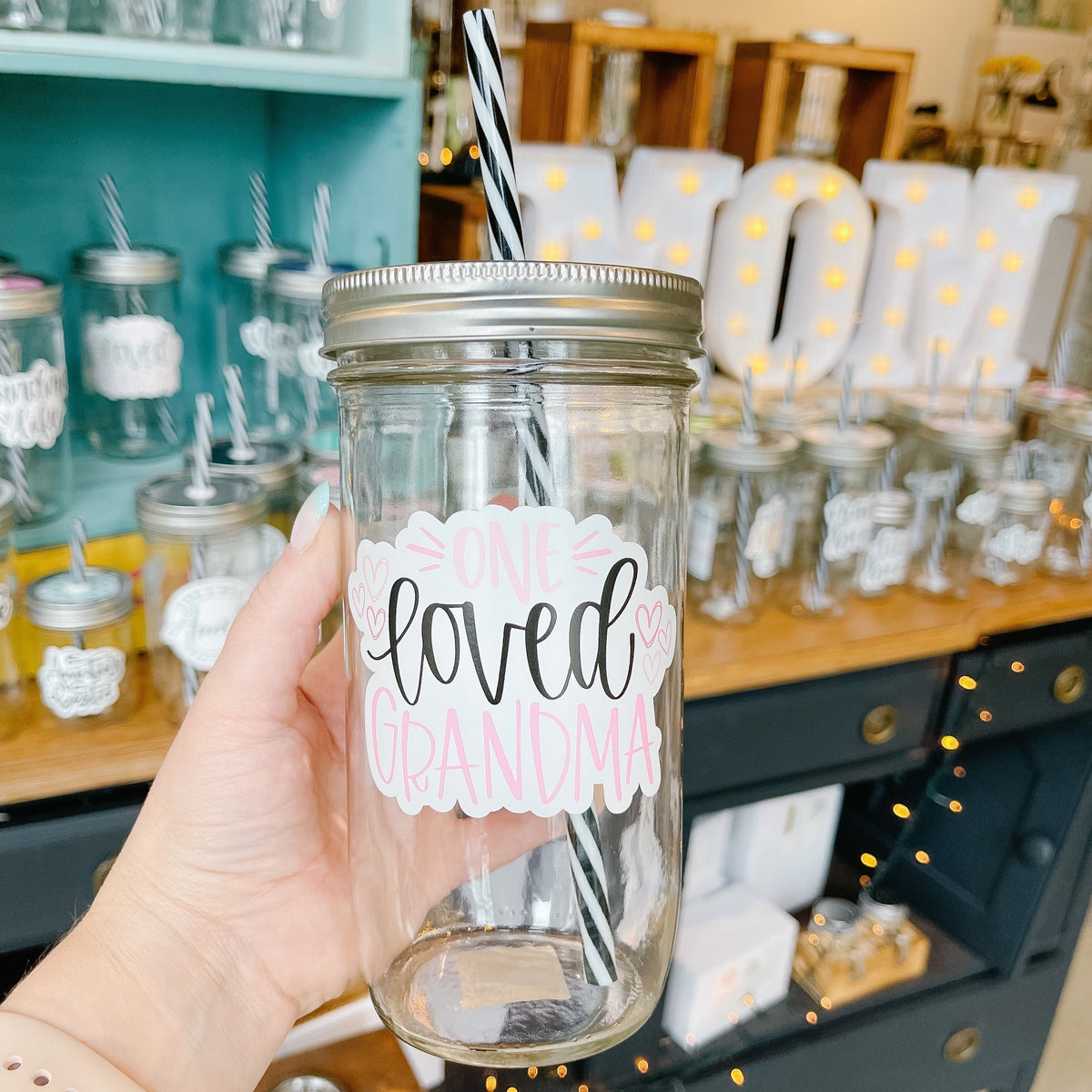 Hand holding a mason jar tumbler that says "one loved grandma” in pink and black