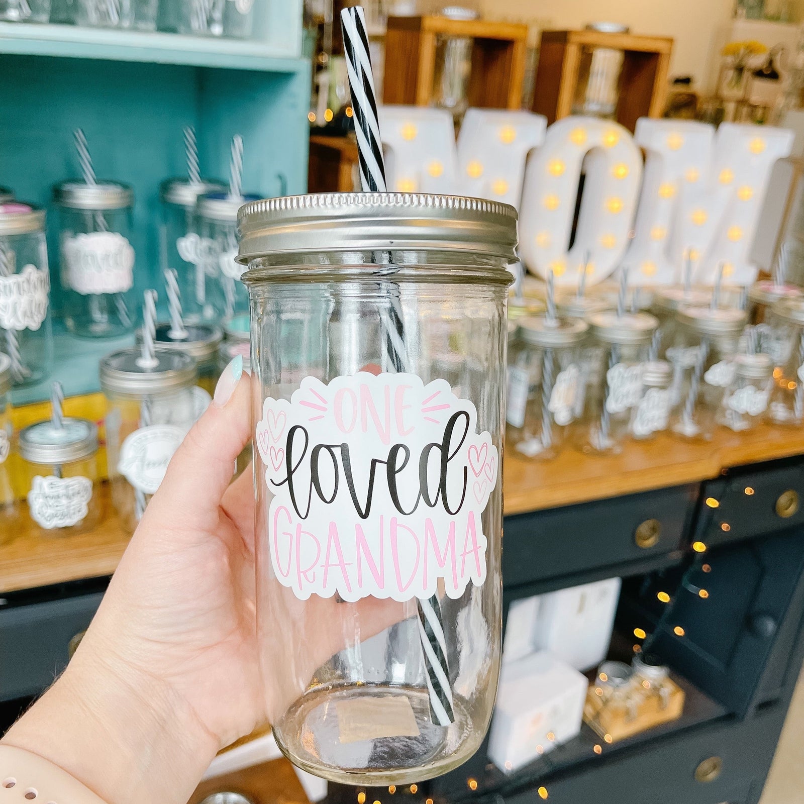 Hand holding a mason jar tumbler that says "one loved grandma” in pink and black