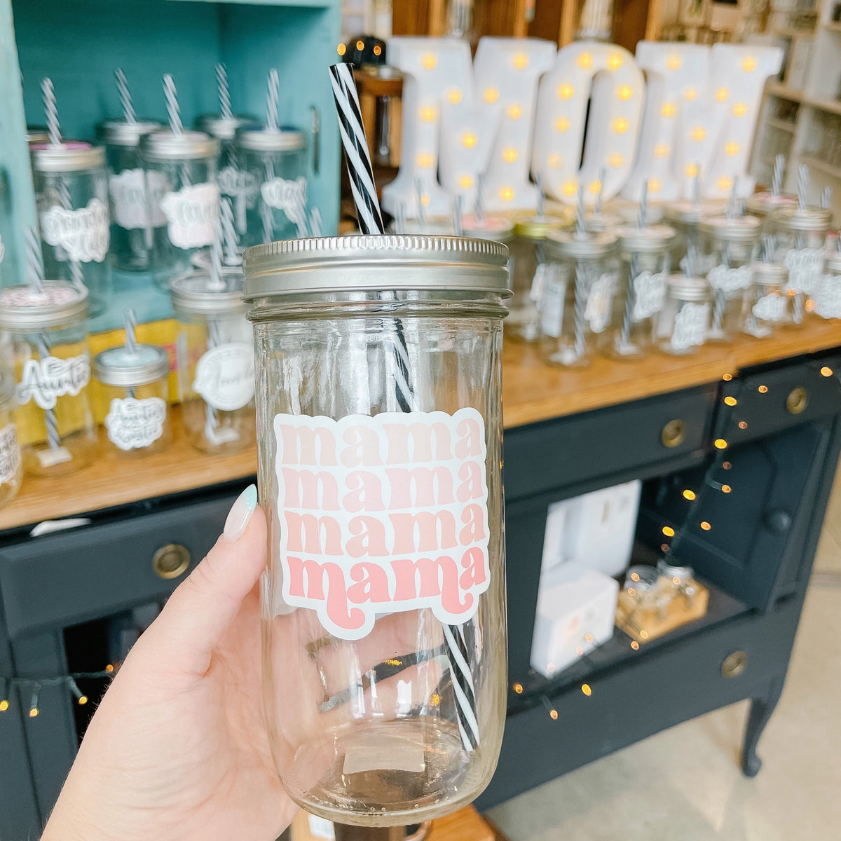 Hand holding a mason jar tumbler that says "mama" in a retro font four times in various shades of pink