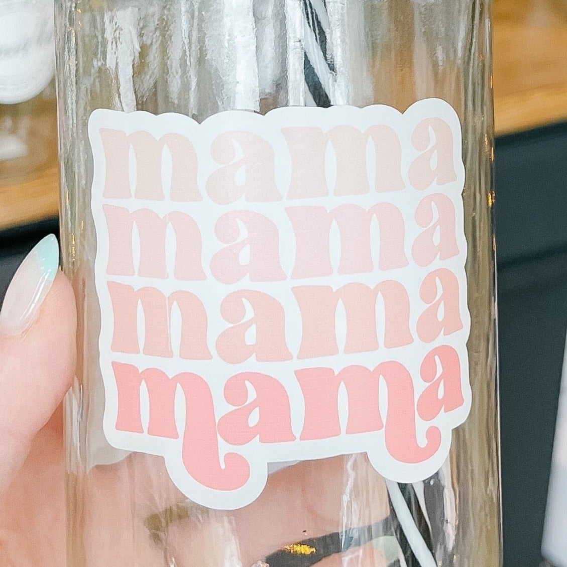 Hand holding a mason jar tumbler that says "mama" in a retro font four times in various shades of pink