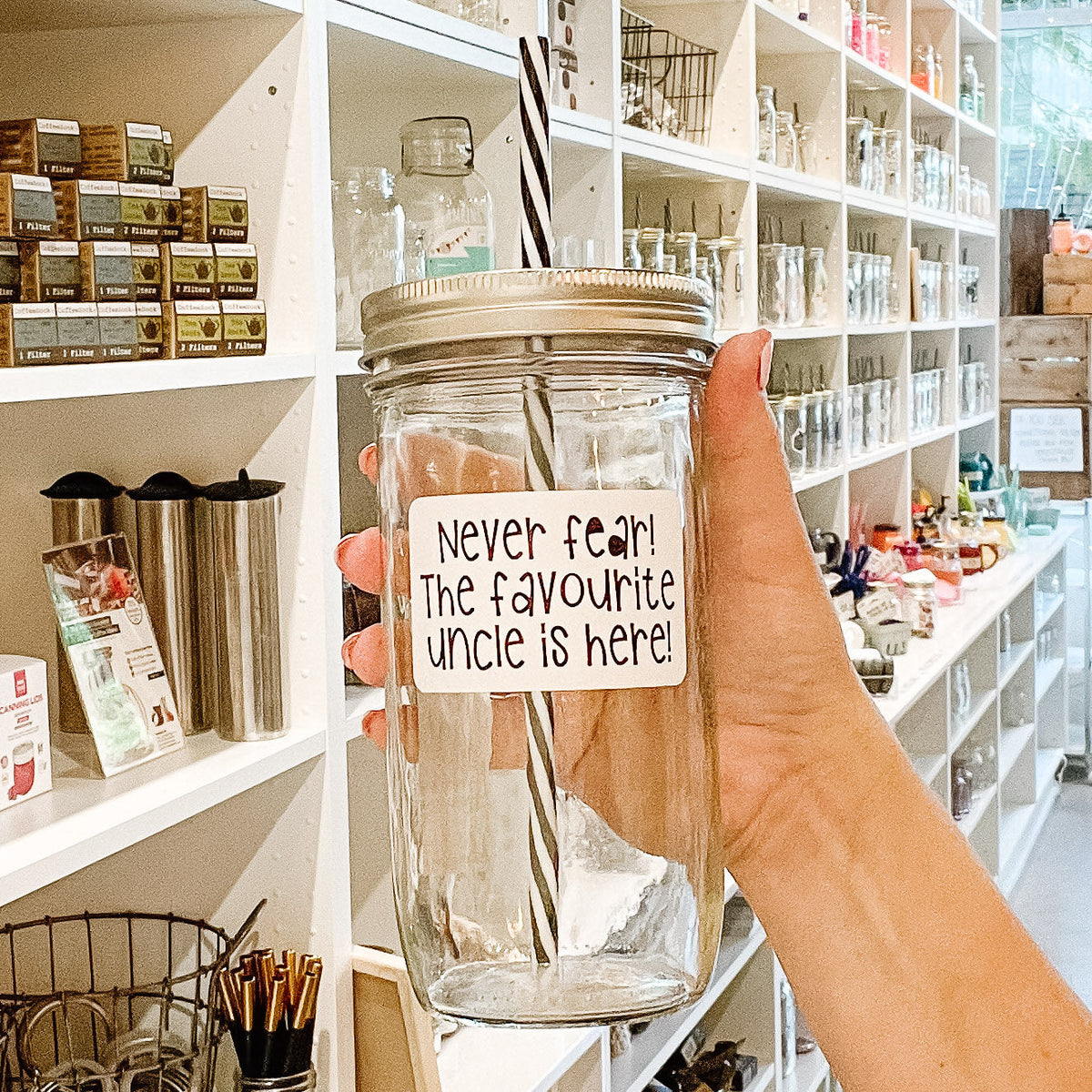 Close up of a hand holding a mason jar tumbler that says “never fear! The favourite uncle is here”