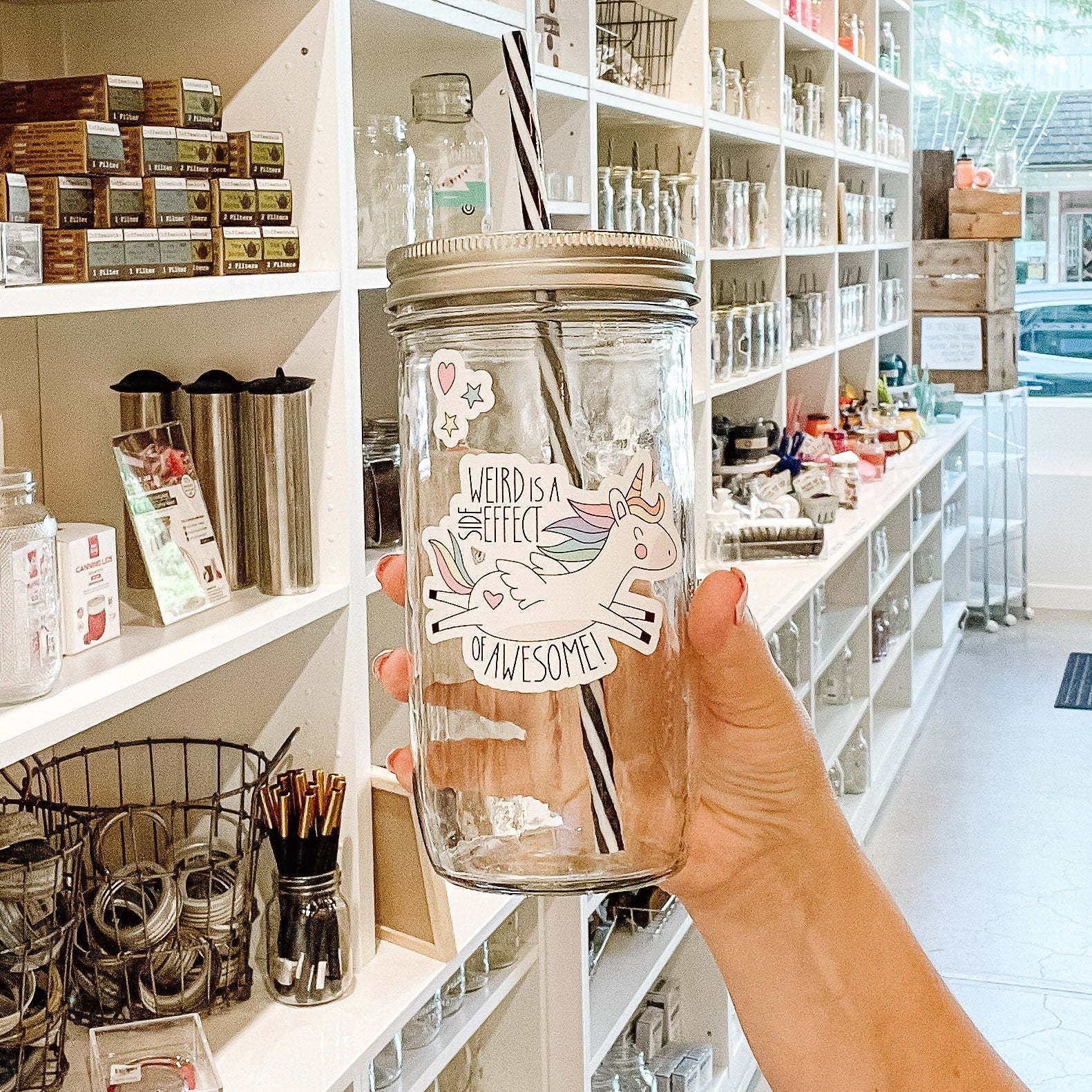 Hand holding a mason jar tumbler that has a picture of a unicorn flying and says "weird is a side effect of awesome"