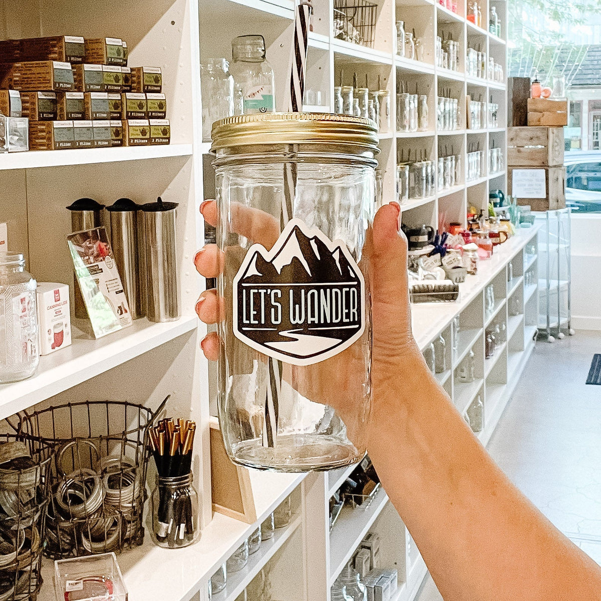 Close up of a hand holding a mason jar tumbler that says “let’s wander” with mountains.