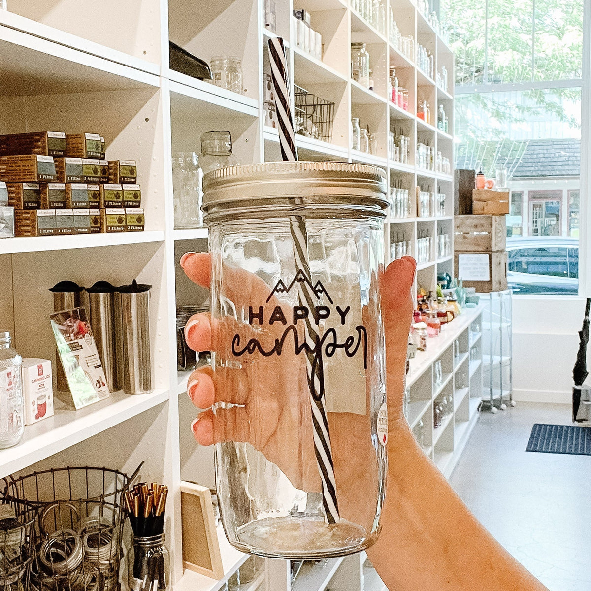 Close up of a mason jar tumbler that says “happy camper” with three mountain peaks