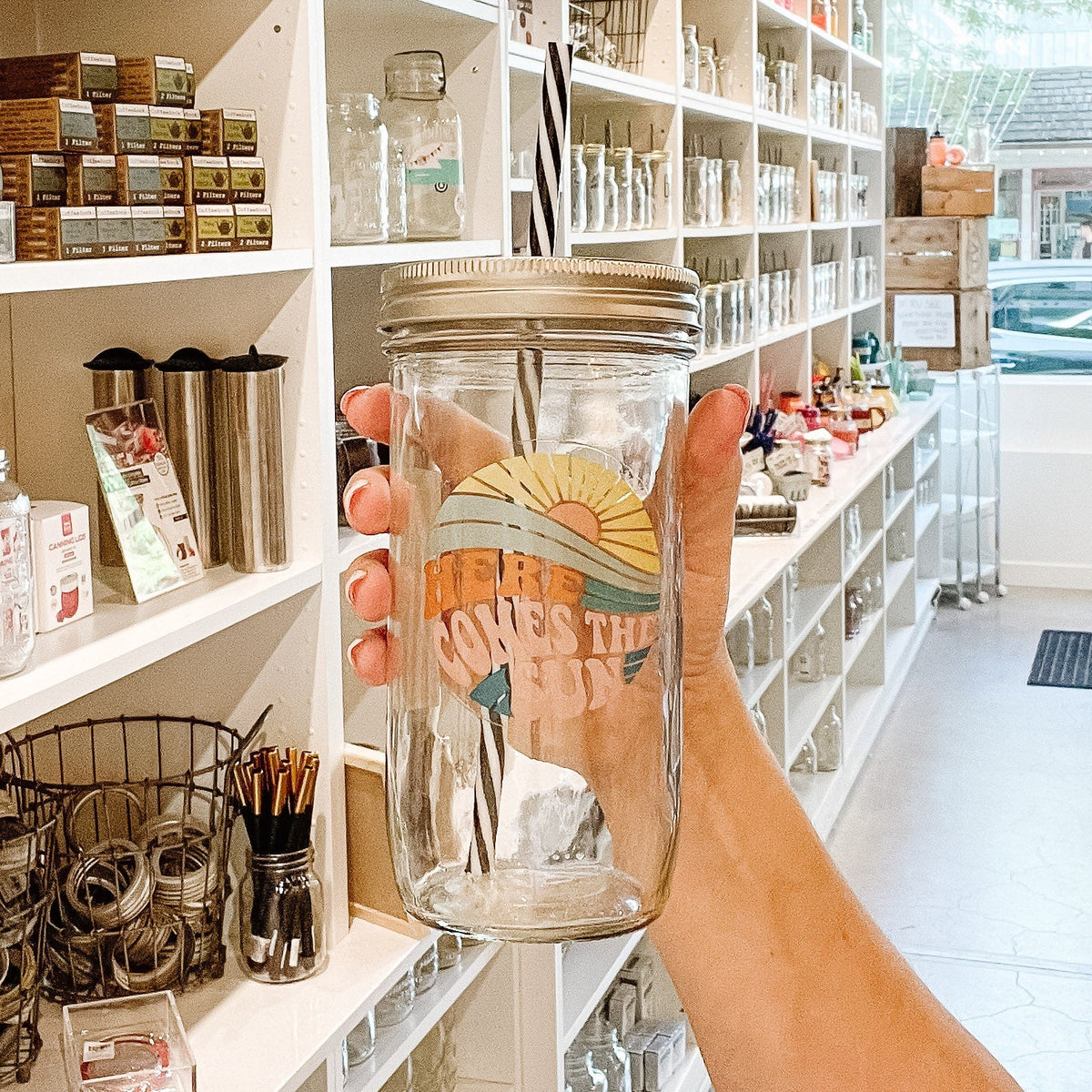 Close up of a mason jar tumbler that has the image of a sun rise and says “here comes the sun”