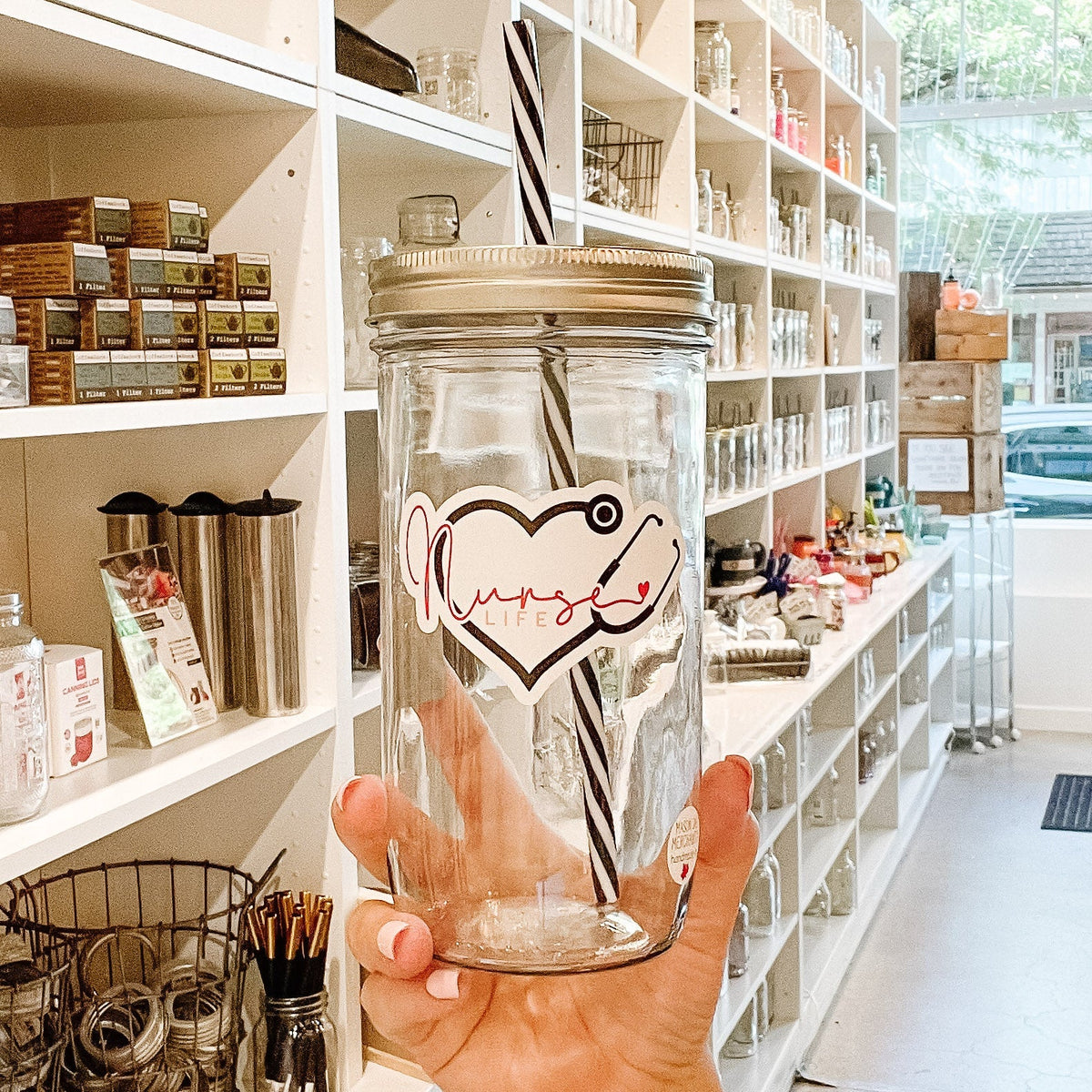 Close up of a hand holding a mason jar tumbler that says "nurse life” within a heart made out of a stethoscope