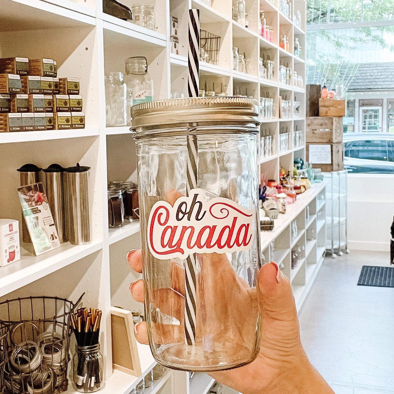 Hand holding a mason jar tumbler that says “oh Canada” in black and red