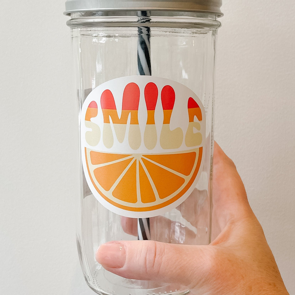 Close up of a hand holding a mason jar tumbler that says “smile” over an orange slice.