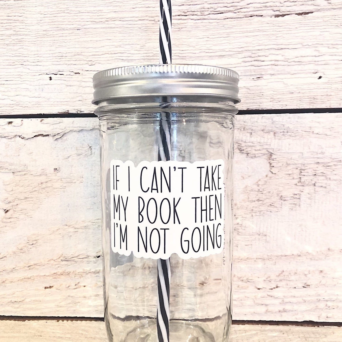 Mason jar tumbler that says “If I can’t take my book then I’m not going” in black lettering on a white background.
