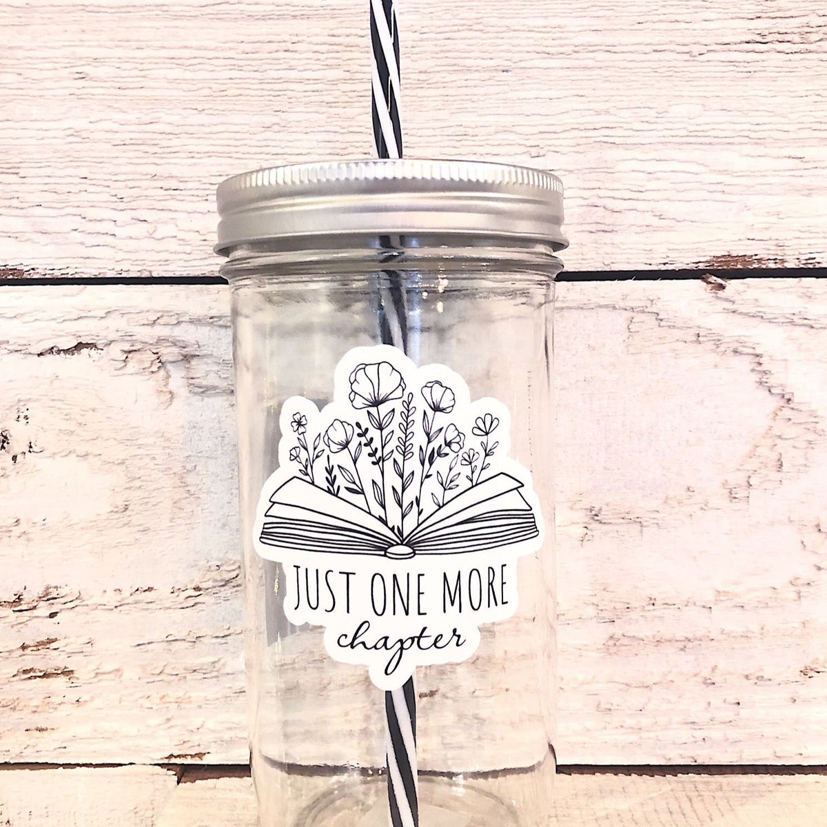 Mason jar tumbler that says “just one more chapter” with flowers growing out of an open book