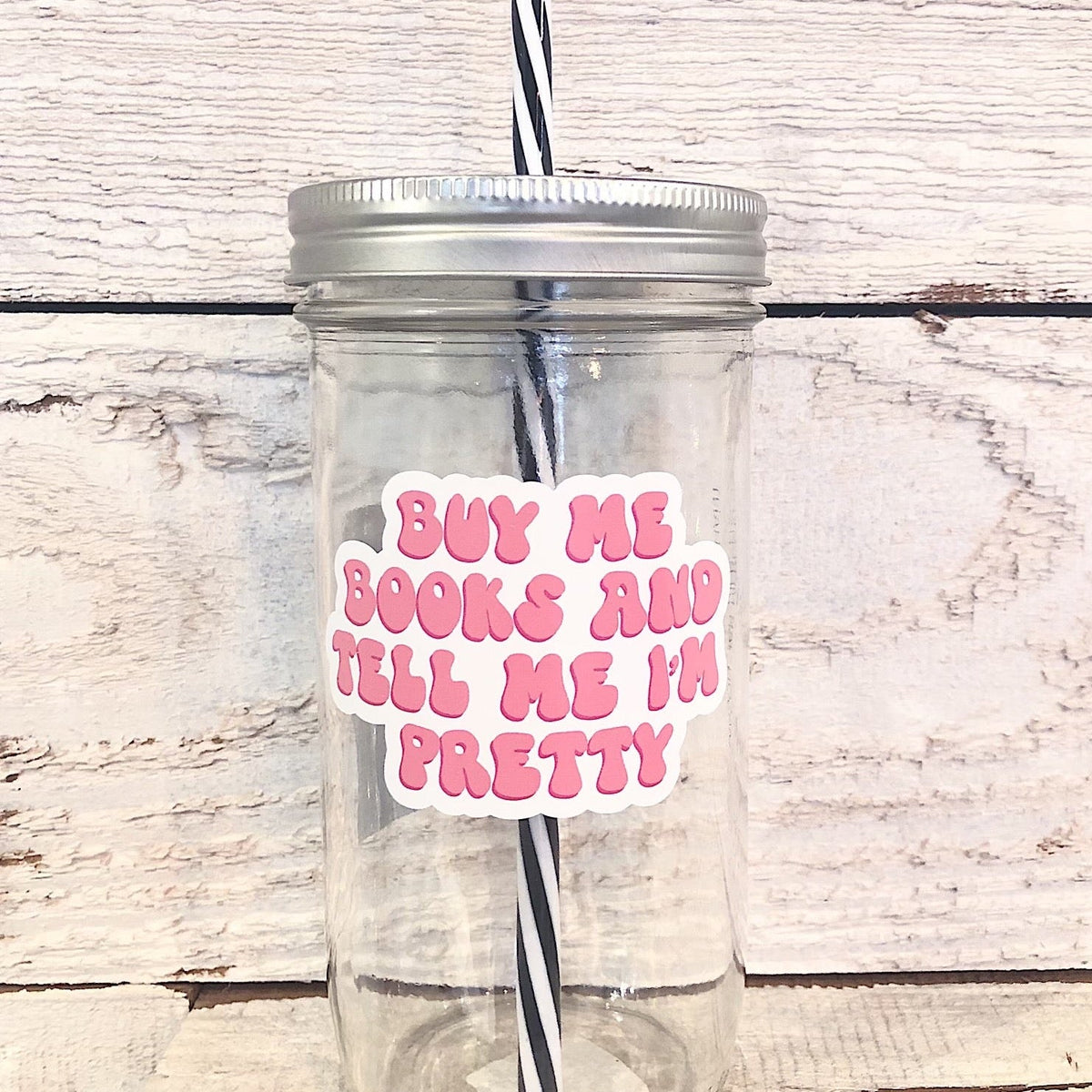 Mason jar tumbler that says “buy me books and tell me I’m pretty” in pink bubble letters on a white background.