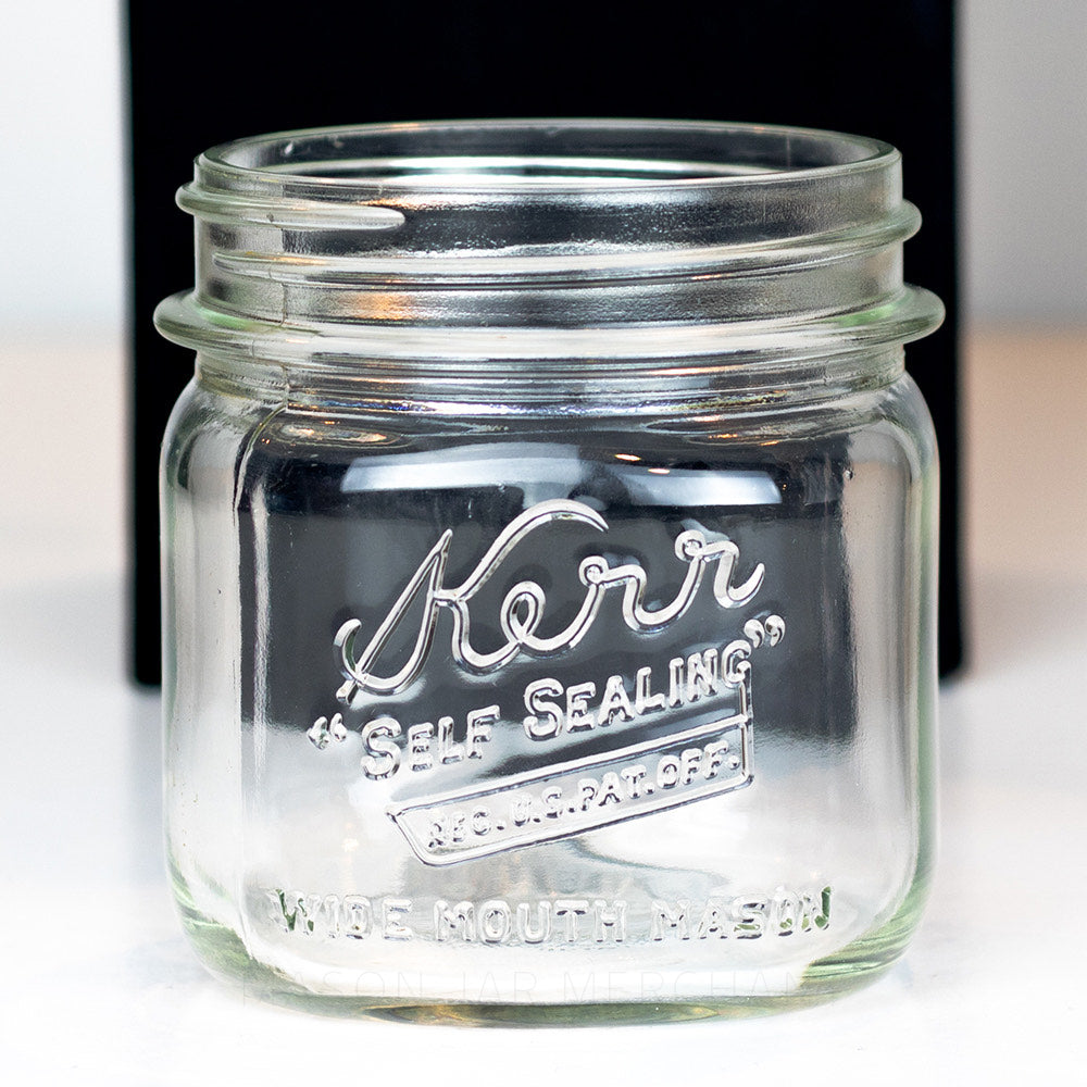 A close up of a Kerr wide mouth pint mason jar with "self-sealing" logo, against a white background