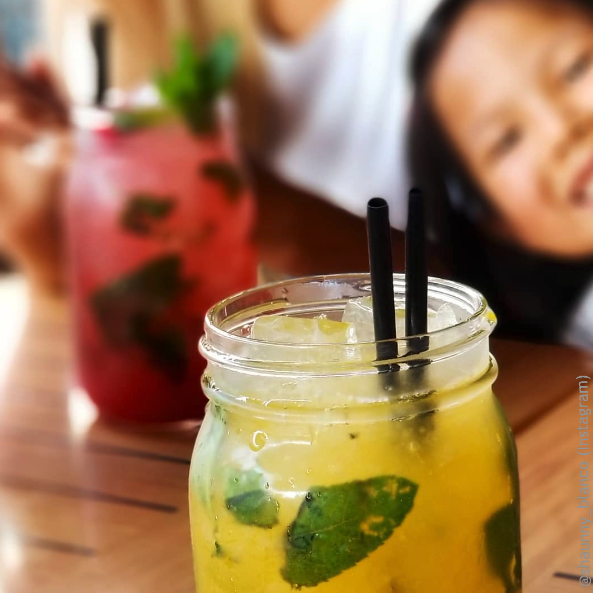 a wide mouth quart mason jar filled with lemon and raspberry juice and two black straws with a smiling little girl on the background