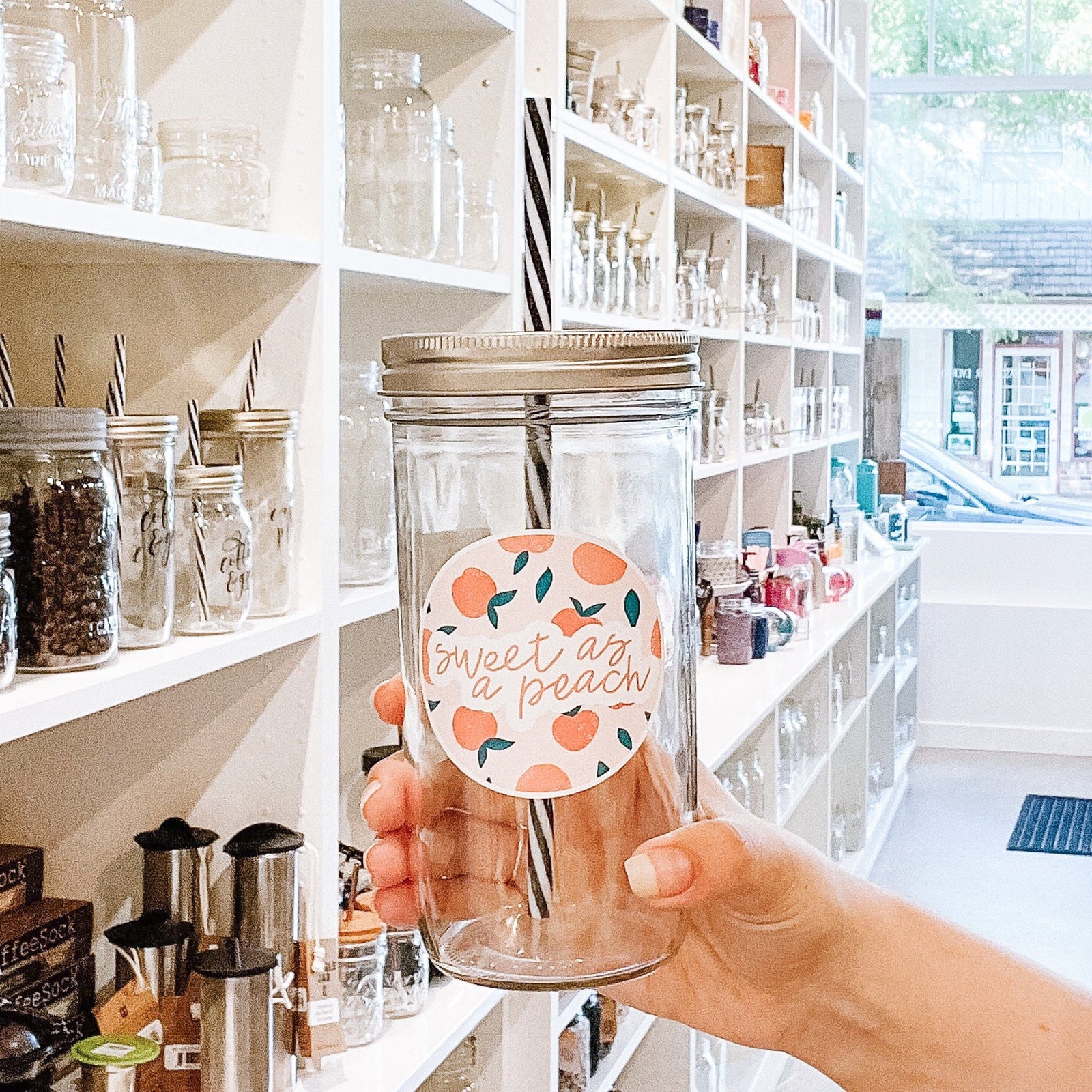 hand holding a mason jar tumbler that says "sweet as a peach" in orange cursive. there is a circular decals behind it that has drawings of peaches on it