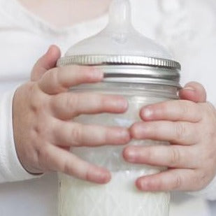 Baby holding a mason jar with silicone nipple filled with breast milk.