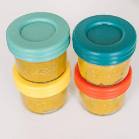 Close up top shot of 4 oz mason jar bottles with baby food and covered with lids in Paprika, Mango, Aqua, and Ocean. All stacked in twos. Photographed in a white countertop.