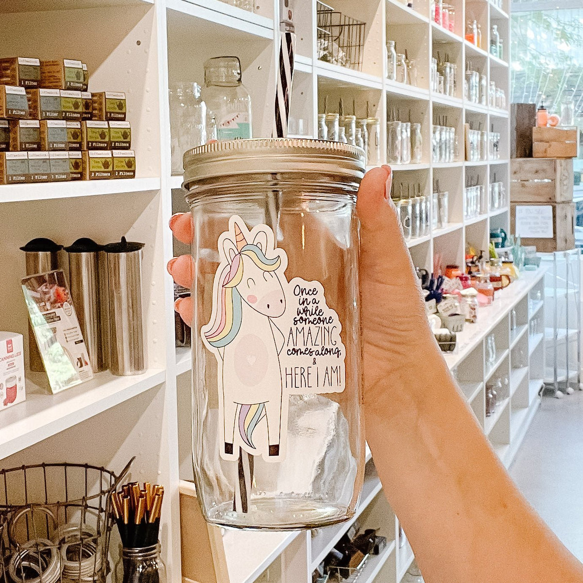 Close up of a hand holding a mason jar tumbler that says “Once in a while someone amazing comes along & Here I am!” With a unicorn to the left of the text.