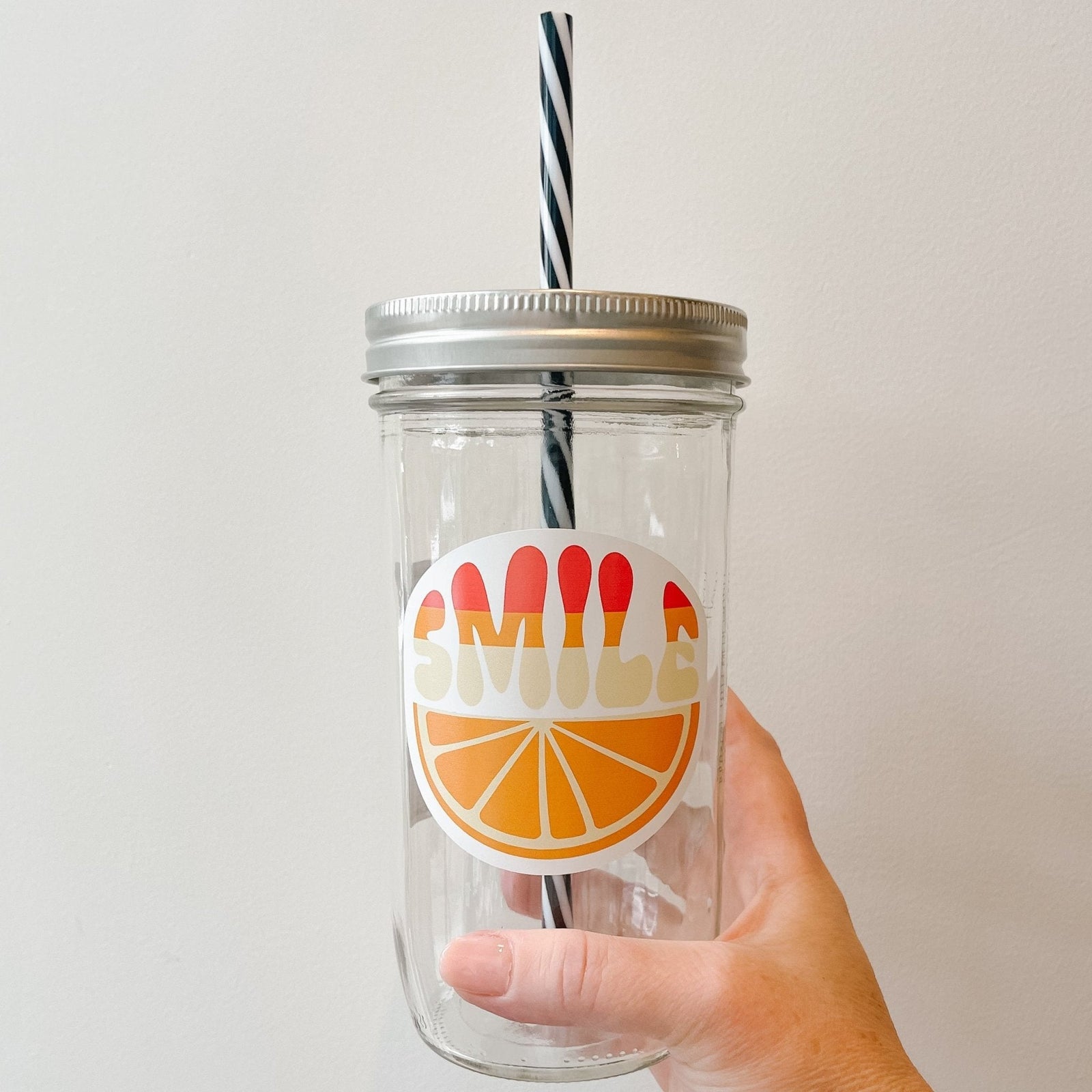 Hand holding a mason jar tumbler that says “smile” over an orange slice.