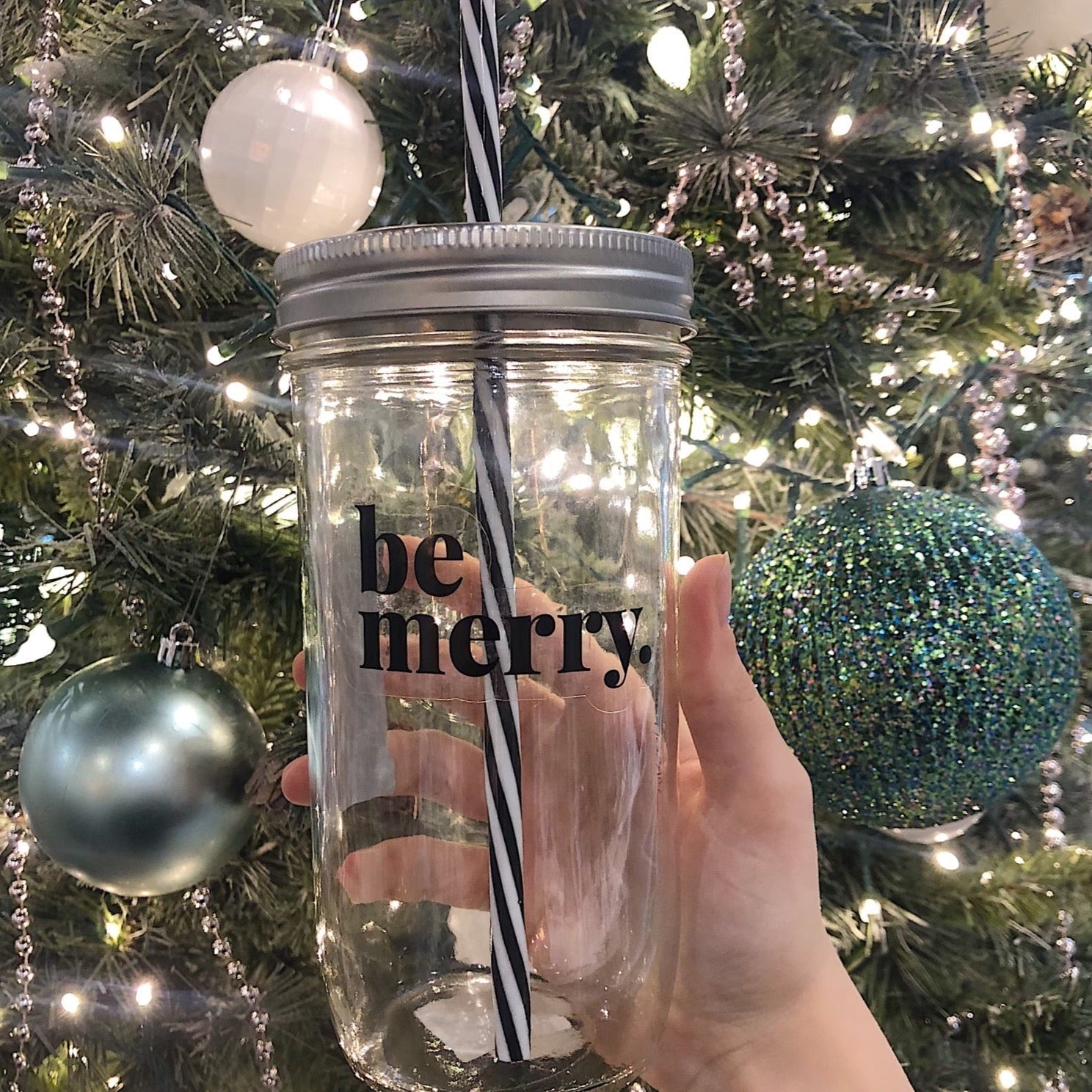 Hand holding a mason jar tumbler that says "be merry.” 
