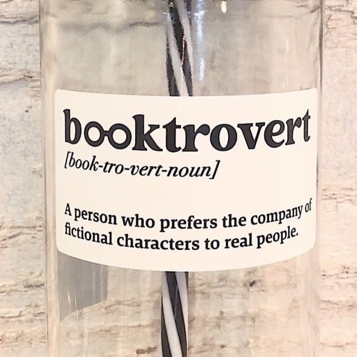 Flat lay of a mason jar tumbler that says “booktrovert. A person who prefers the company of fictional characters to real people”, and straw lid with a repeating pattern of a pink lamp, and a black and white striped straw. 