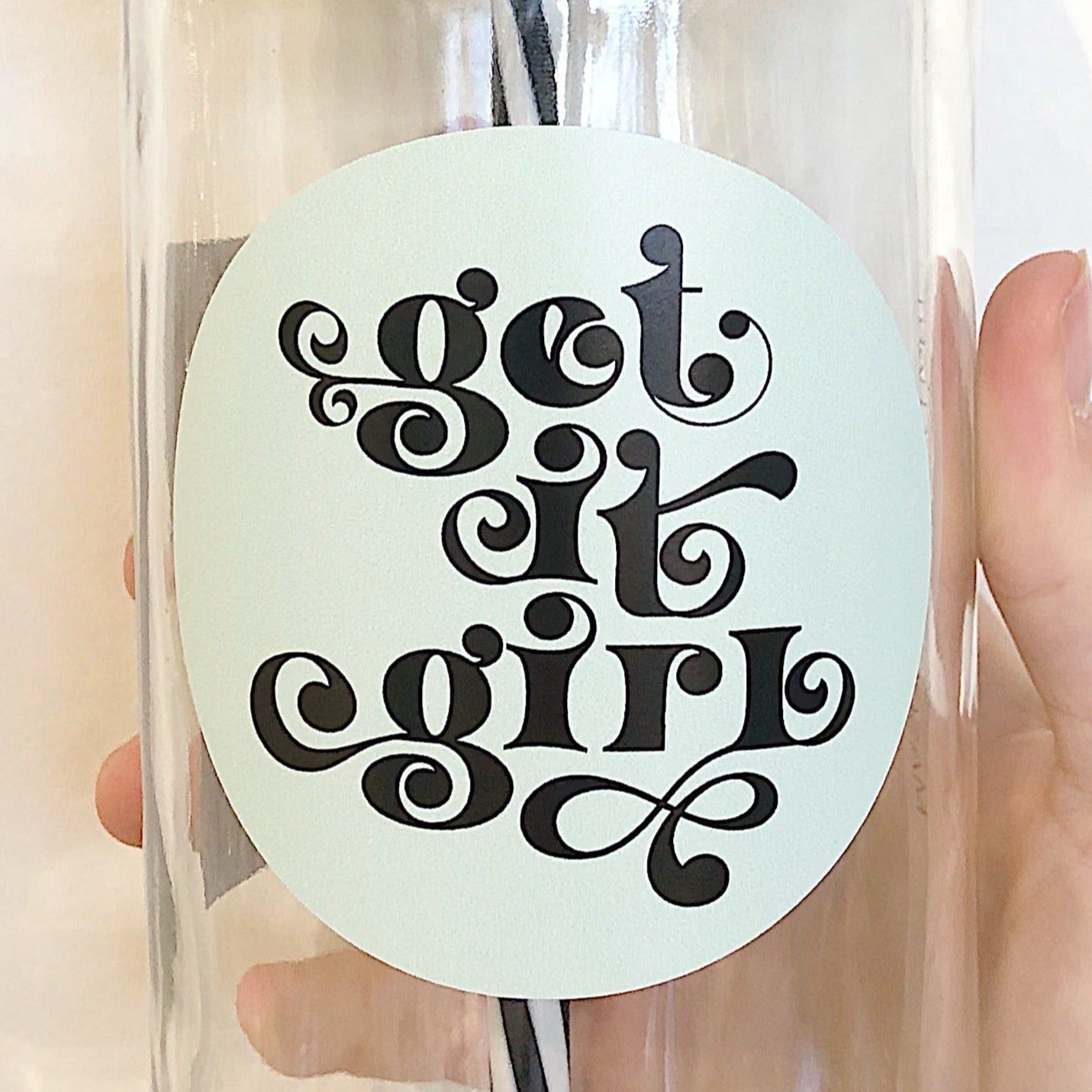 Hand holding a mason jar tumbler that says “get it girl” in black on a light mint circular background. 