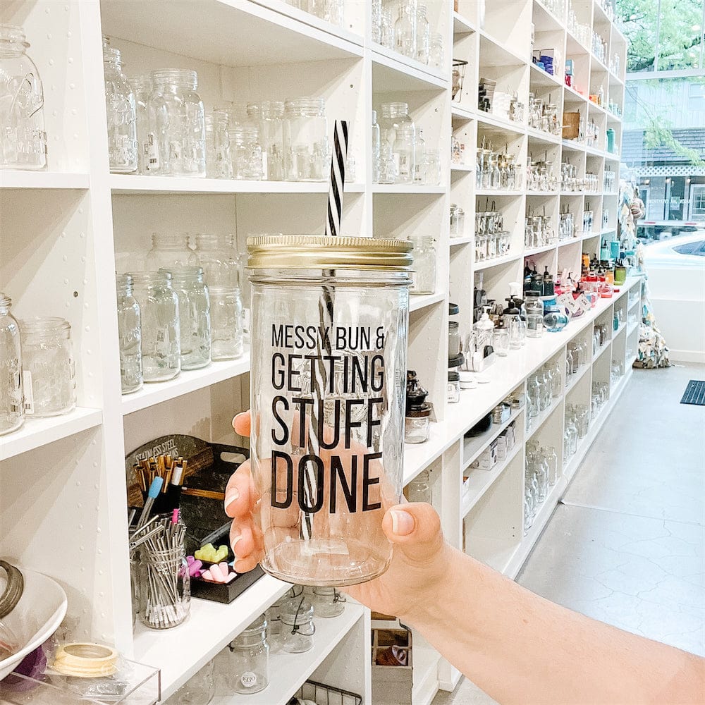 Wide angle of a hand holding a mason jar tumbler that says “messy bun &amp; getting stuff done”