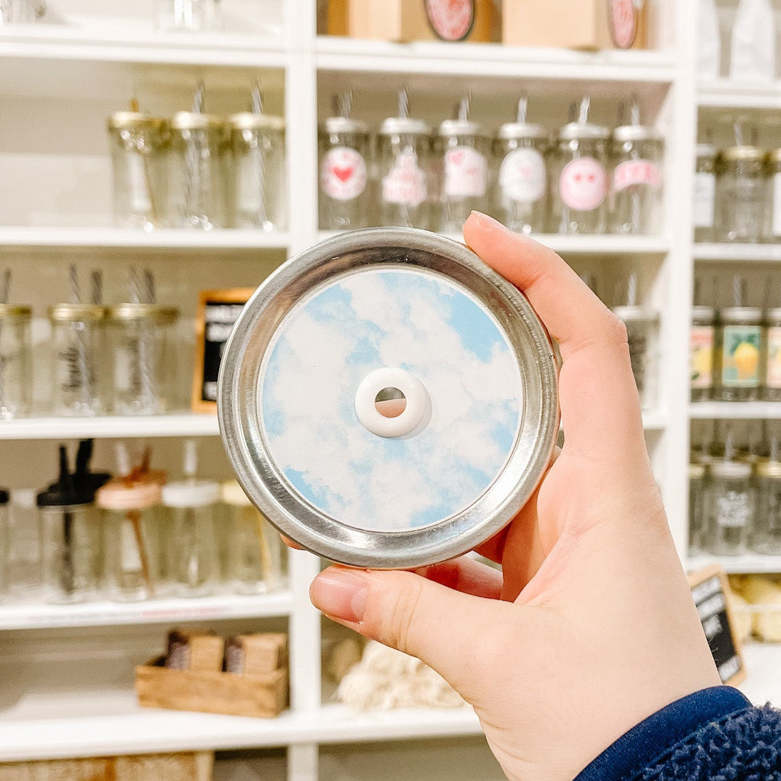 Hand holding mason jar patterned straw lid with a cloudy watercolour design on light blue background 