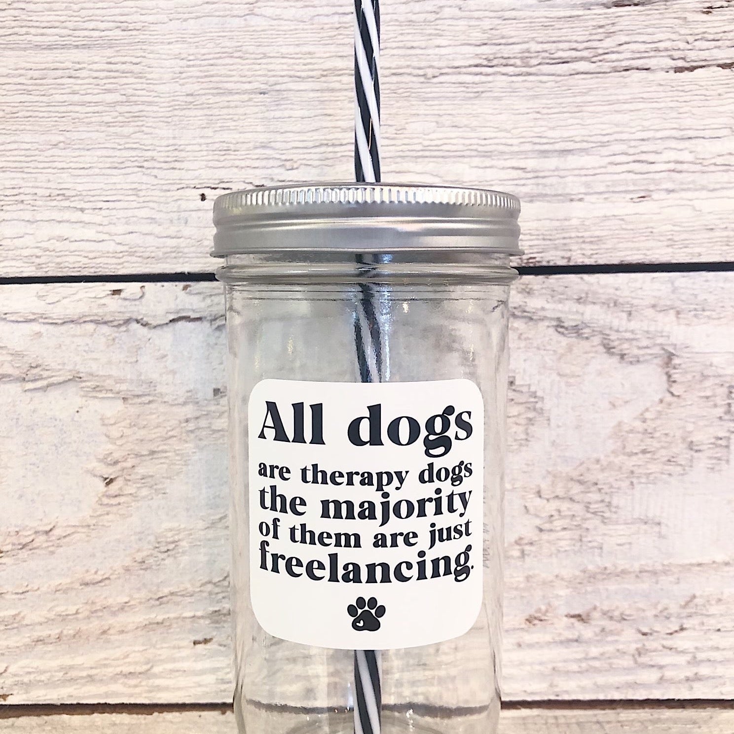 A mason jar tumbler that says “All dogs are therapy dogs the majority of them are just freelancing.” In black letters on a white background with a small black paw print at the bottom.