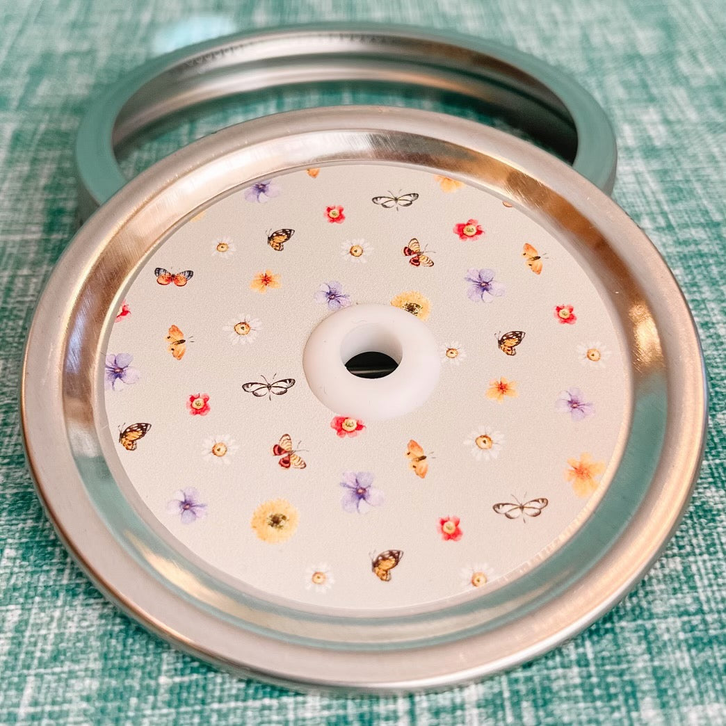 straw lid with a pale green background there are flowers and butterflies arranged in a grid-like pattern