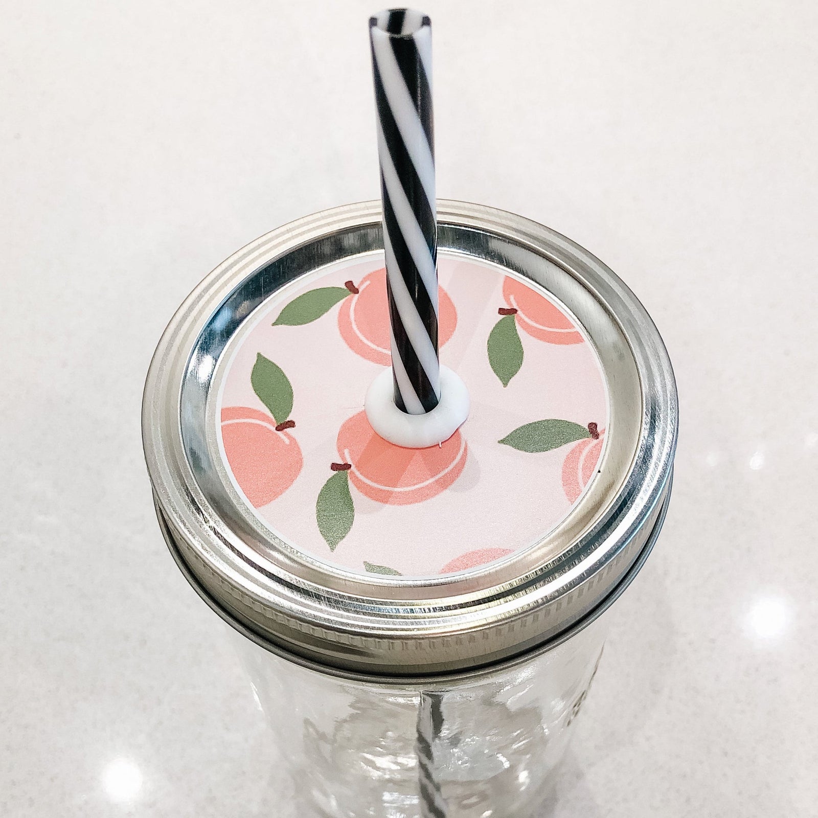 Hand holding patterned mason jar straw lid that has peaches on pale pink background