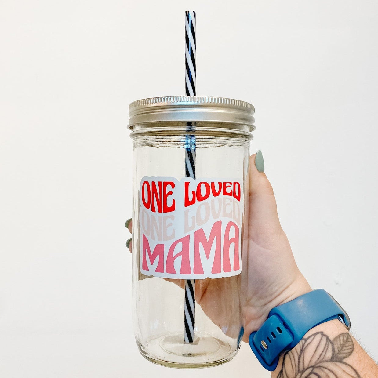 hand holding a mason jar tumbler that says "One Loved One Loved Mama" the first 'one loved' is in red, second in like ink, and the 'mama' in pink. Font is a wavy retro vibe