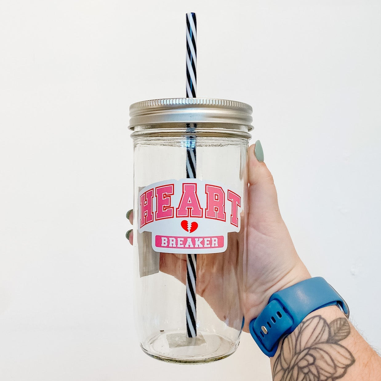 hand holding a mason jar tumbler that ays "HEART" in blocky varsity style letters and "BREAKER" below it, with a small broken heart between the words